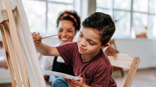 Teacher assisting a child with Down syndrome - painting class on canvas 